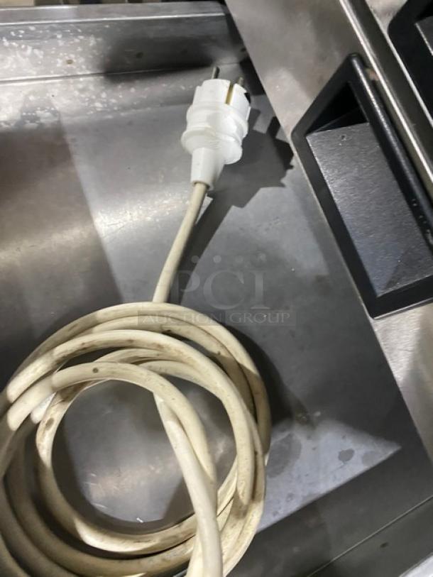 Coiled white power cord on a stainless steel surface, part of a commercial display case unit.