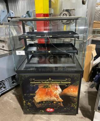 Commercial black curved glass refrigerated display case with multi-tier shelving for gourmet desserts, branded with "Authentic Turkish Gourmet Desserts" by Ipek.