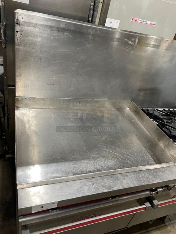 Vulcan commercial stainless steel flat griddle with split top, 4-burner range, and double oven combo. Includes back splash and wired oven racks. In used condition on legs.