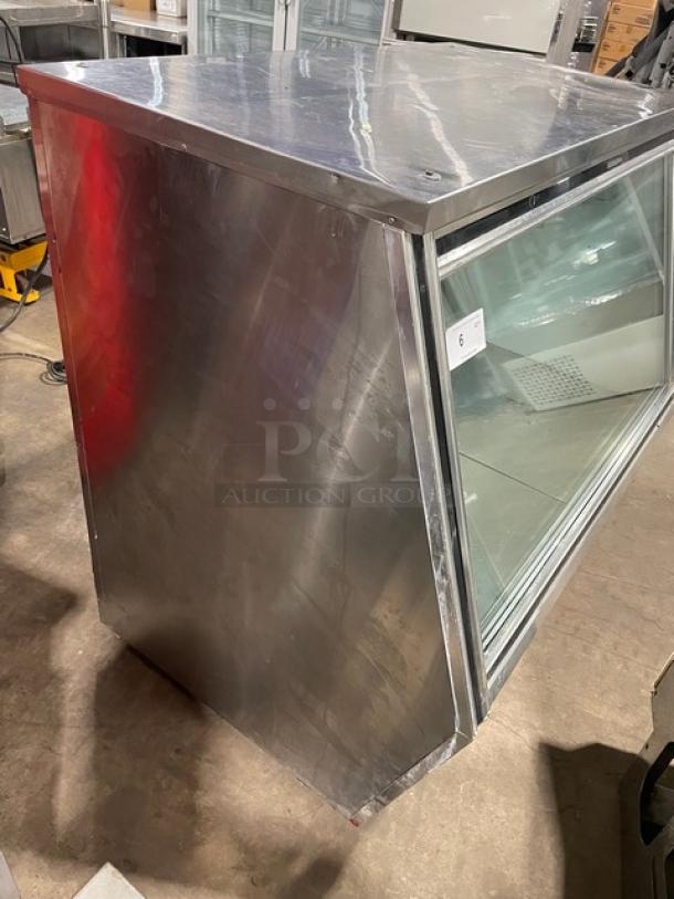 Leader stainless steel refrigerated meat/deli merchandiser with slanted glass, rear sliding doors, and storage compartment.