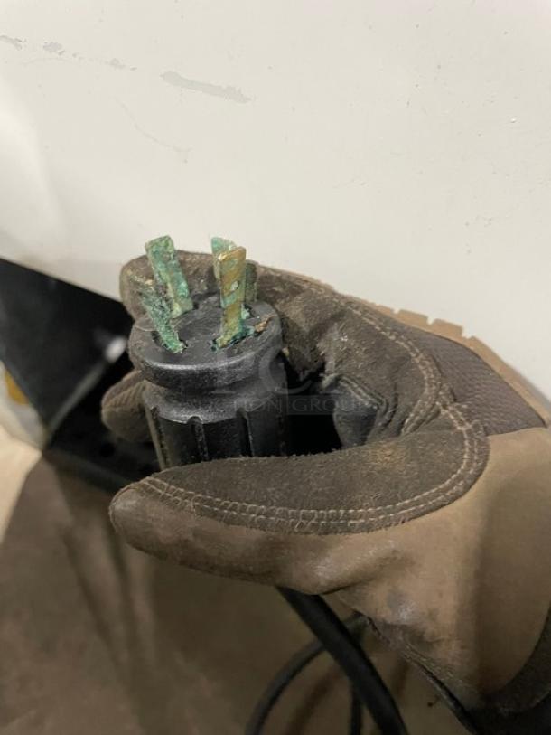 Close-up of a gloved hand holding a corroded plug for a True GDM-72F commercial freezer. Plug shows wear and oxidation.