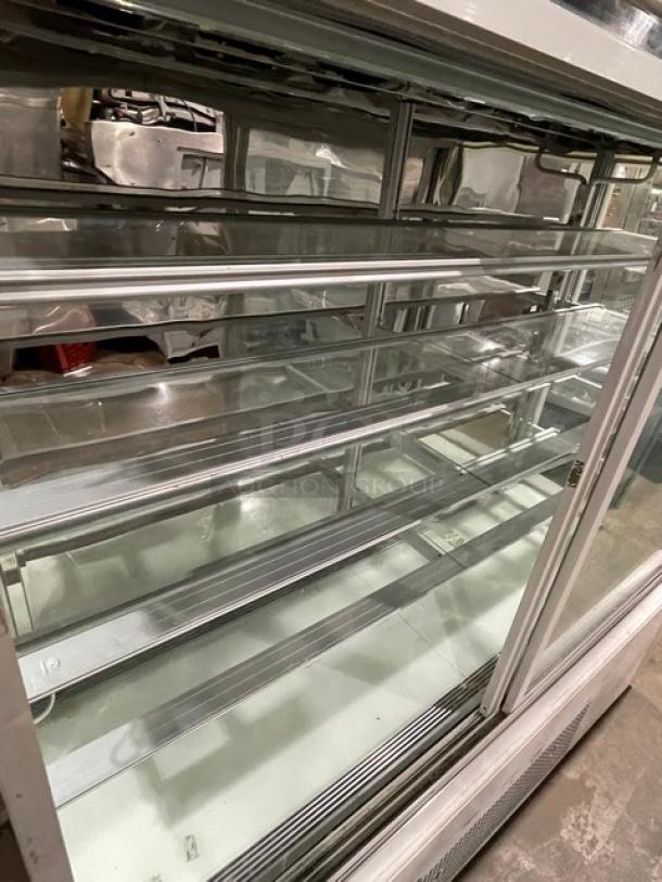 Commercial white refrigerated bakery display case, multi-tiered, straight glass, with double sliding doors, on casters.