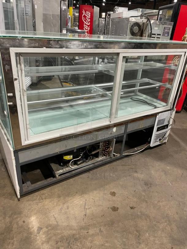 Commercial white glass refrigerated bakery display case with multi-tier shelves and rear double sliding glass doors. Visible cooling unit.