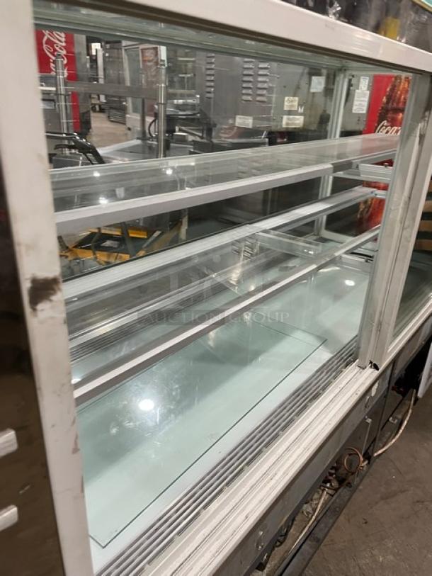 Commercial white glass refrigerated bakery merchandiser with multiple tiers, rear sliding glass doors, in good condition.