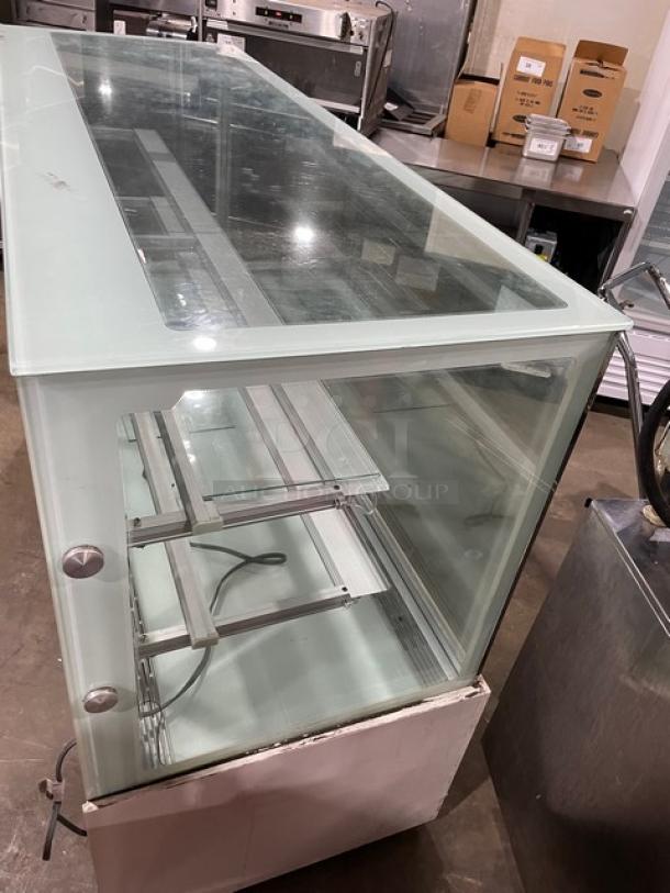 Commercial white glass refrigerated bakery display case with multi-tier shelving and rear double glass sliding doors.