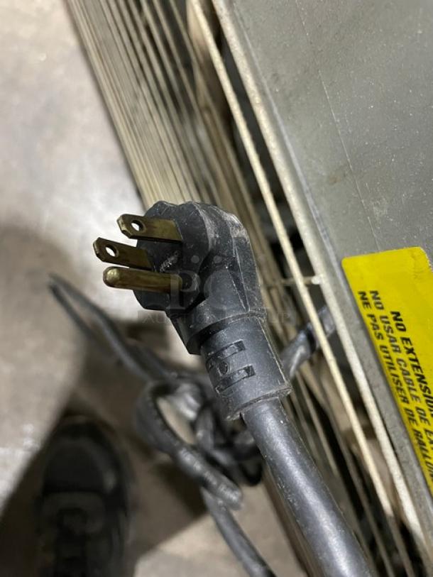Close-up of a power plug and cord for an Imbera VRD37C02 commercial refrigerator, showing prongs and a safety label.