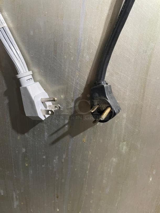 Two power plugs against the stainless steel surface of a Delfield/Alco commercial refrigerator/freezer combo.