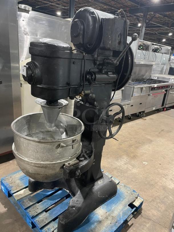 Commercial black electric-powered heavy-duty planetary mixer with stainless steel bowl, spiral dough hook, and sturdy legs.
