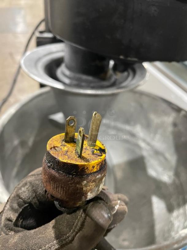 Commercial black heavy-duty planetary mixer, features stainless steel mixing bowl, spiral dough hook, on legs, with electric plug shown.