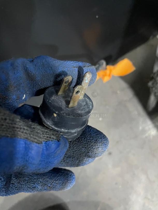 Close-up of a power plug for a Habco ESM28 commercial refrigerator, 115V, shown held by a gloved hand.