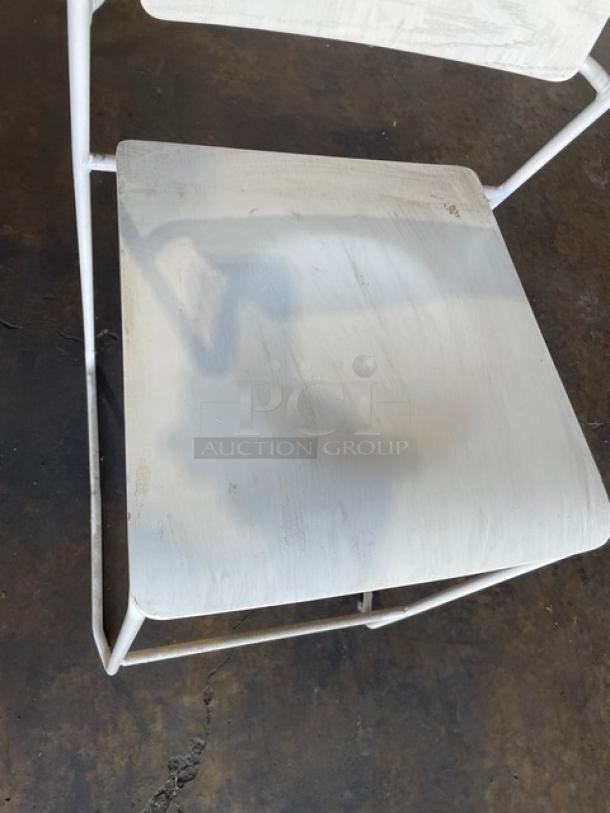 White wooden-style dining chair with metal frame, stackable for indoor-outdoor use. Visible wear on seat surface.