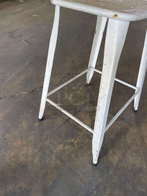 Distressed white metal stackable bar-height stool for indoor-outdoor use. Visible wear adds rustic charm.