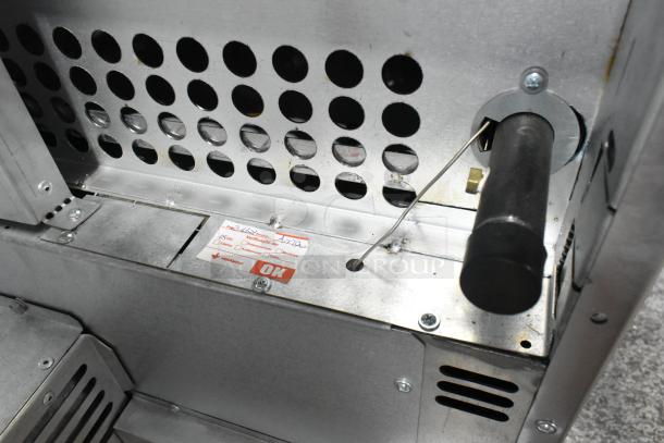 Inside view of 2021 Venancio R602CO-60B commercial gas range with inspection label, showing metal construction and ventilation holes.
