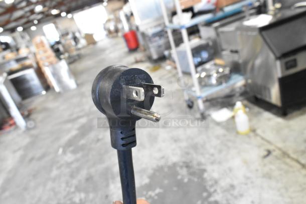 Close-up of a three-prong plug for the True T-19F-HC stainless steel commercial reach-in freezer. Background shows warehouse equipment.