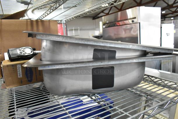 2 new scratch and dent stainless steel single bay drop-in sinks on a metal shelf, items part of an auction lot.
