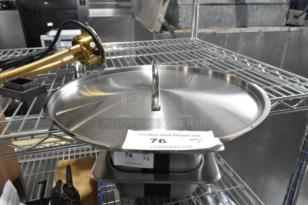 Brand new stainless steel round lid with scratches and dents, shown on a metal rack. Label displays "76" for auction reference.