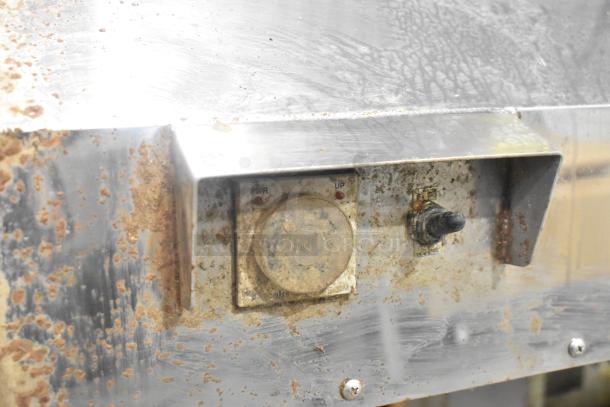 Metal commercial floor marinating station with visible dial and switch, showing signs of rust and wear on the metal surface.