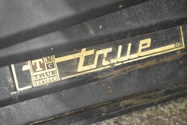 True GDM-49EM metal cooler label, showing brand and manufacturer details. Surface shows signs of wear.