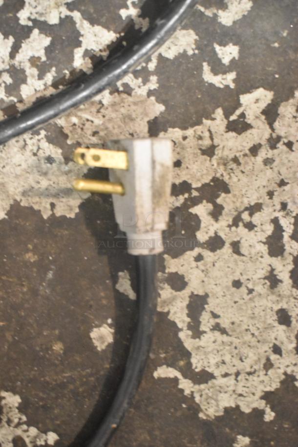 Close-up of a power cord plug on a worn floor surface, possibly related to an appliance.