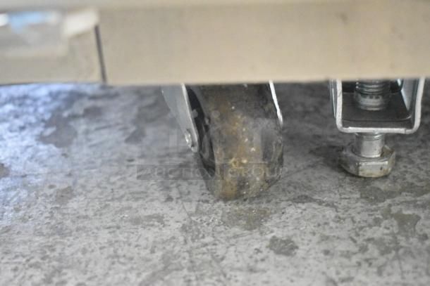 Worn caster wheel of a Unique stainless steel commercial cooler/freezer, highlighting mobility feature.