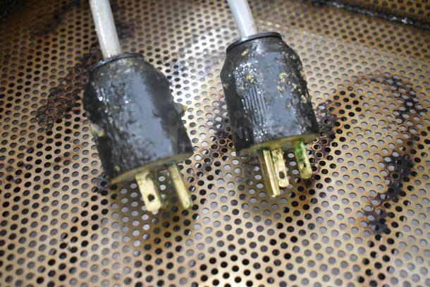 Close-up of two electrical plugs with a worn appearance on a perforated metal surface.