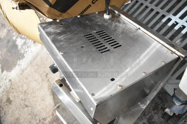 Stainless steel commercial countertop waffle maker in used condition, visible scuffs, vented top panel, and control knob on side.