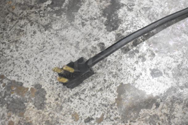 Close-up of a power cord plug for Beverage Air SPE72HC-18 prep table, showing three prongs on a concrete floor.