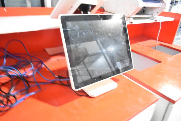 White and red counter with POS monitor, slightly used. Visible cables. Ideal for retail settings.