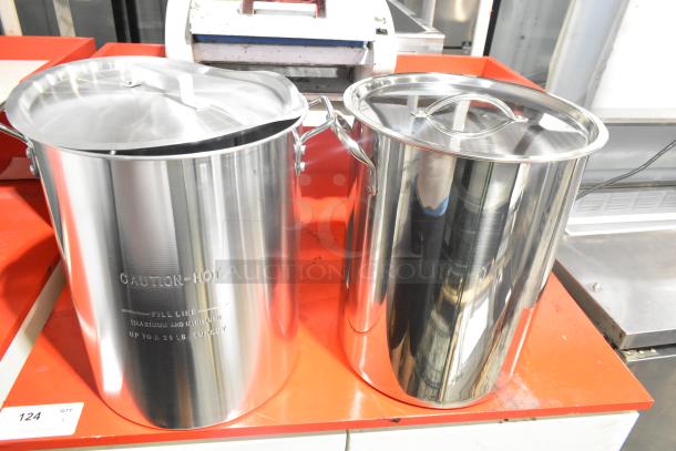 Two brand new stainless steel deep fat fryer stock pots with lids, caution label, and fill line markings. Slight scratch and dent.