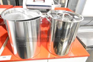Two brand new stainless steel deep fat fryer stock pots with lids, caution label, and fill line markings. Slight scratch and dent.
