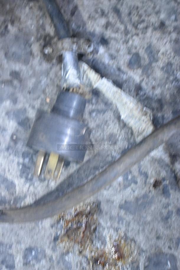 Blurry image showing a power plug against a textured background. Possible wear visible on wiring.