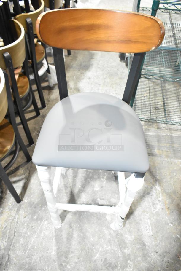 Black metal bar-height chair, brand new, with a wooden backrest and gray cushion seat. Some minor scratches.