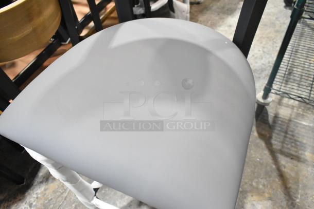 Black metal bar height chair with a wooden backrest and gray cushion seat, new with minor scratches and dents.