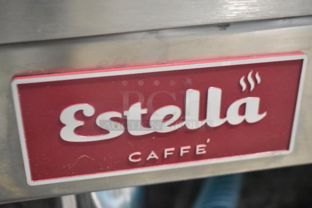 Estella ECEM2/N2 espresso machine badge, red with white text "Estella Caffé," stainless steel background.