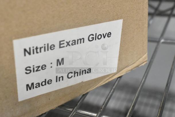 Box labeled "Nitrile Exam Glove, Size: M, Made in China" on a metal shelf, part of assorted new glove lot for auction.