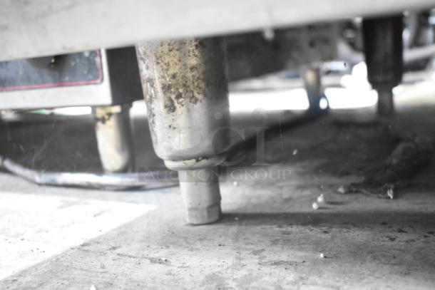 Underneath view of an Imperial stainless steel commercial griddle, showing legs with visible wear and surface dirt.