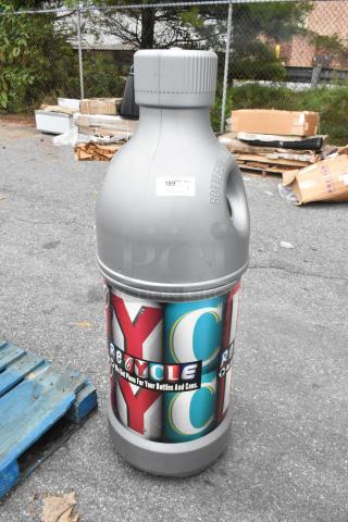 Gray bottle-shaped recycling bin with colorful "Recycle" label for bottles and cans. Outdoor setting, slight wear visible.