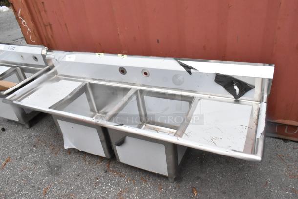 Brand new Regency 600S21818218 stainless steel 2-bay sink with dual drain boards, visible scratches and dents.
