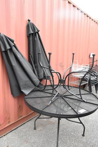Two black metal mesh round patio tables with two black patio umbrellas, good condition, stacked outdoors.
