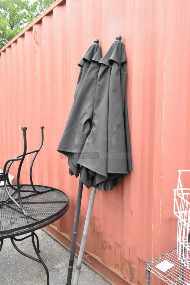 2 black metal mesh round patio tables with 2 black patio umbrellas, in good condition, near a red container.