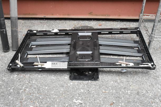 Black metal unit on pavement, horizontal support bars, visible mounting hardware, some surface wear, auction tag 193.