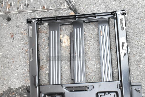 Black metal unit frame on pavement, featuring parallel grooves and slots, showing minor scratches, no visible labels.