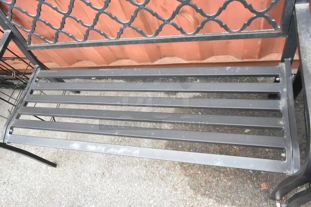 Two black metal benches with armrests, featuring slatted seats and decorative backrest details. Slightly weathered condition.