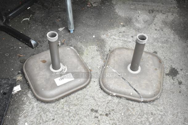 Two metal patio umbrella bases, one with visible crack, both labeled "199." Used condition.