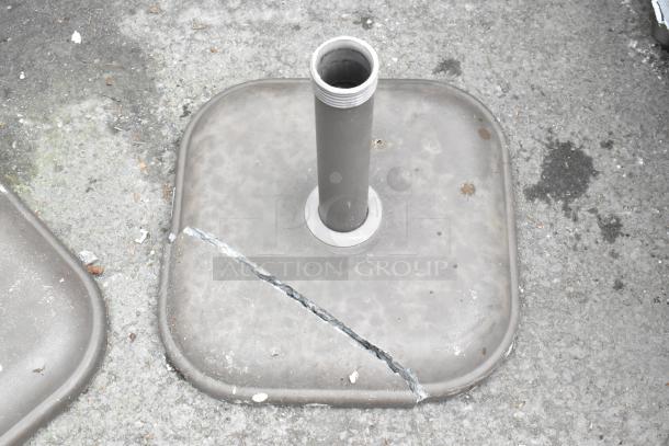 Two patio umbrella bases, one showing a crack. Made of concrete, suitable for outdoor use. Note damage for condition assessment.