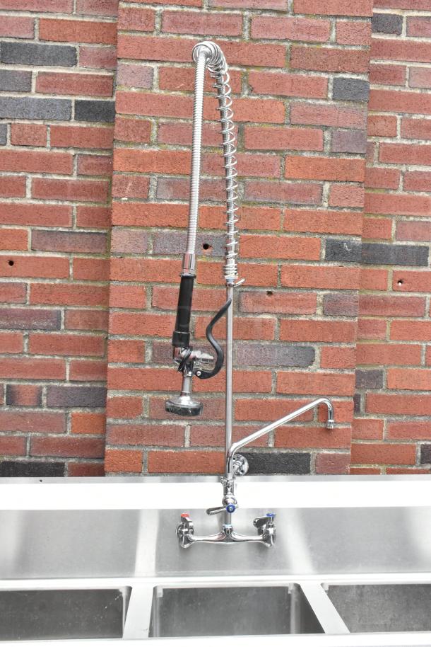 Regency 600S31416212 stainless steel 3 bay sink with dual drain boards, faucet, and handles, brick wall backdrop.