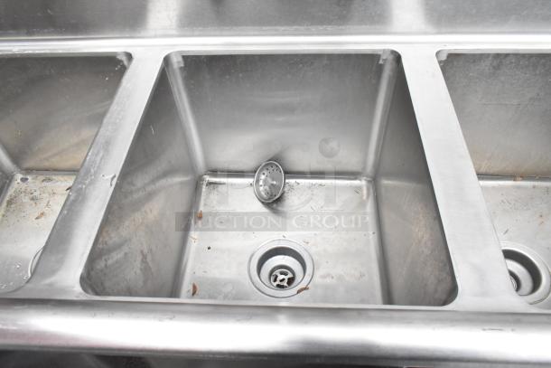 Regency 600S31416212 stainless steel 3 bay sink with dual drain boards, faucet, handles, and visible signs of use.