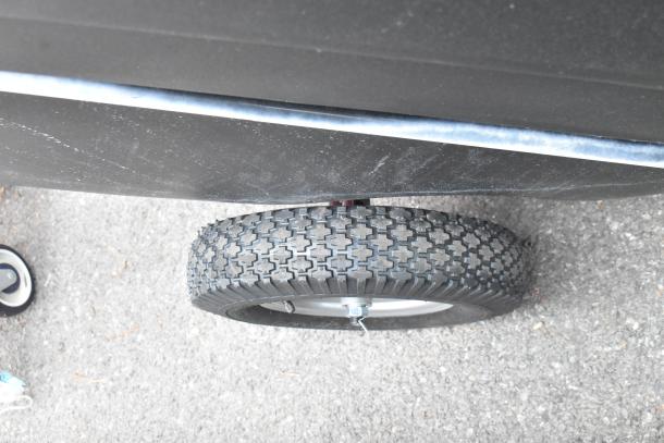 Brand new black poly tilt truck, wheel detail shown; minor scratches visible on surface; ideal for heavy-duty use.