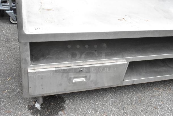 Stainless steel commercial equipment stand with under shelves and two drawers, showing some wear, suitable for kitchen use.