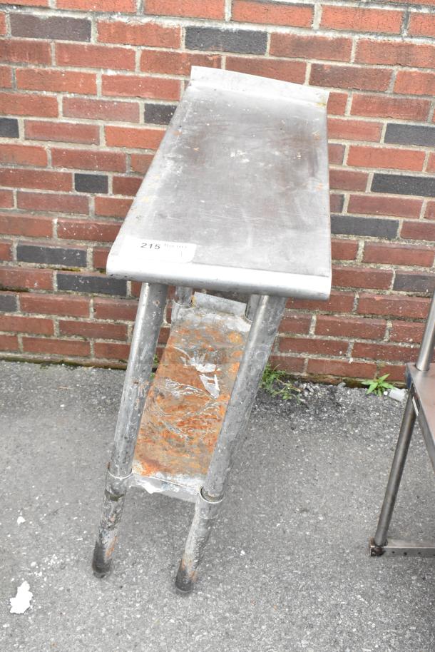 Stainless steel table with undershelf, showing wear and rust. Label marked "215." Ideal for utility or storage use.